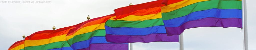 Several LGBTQI+ pride flags fly in the wind.