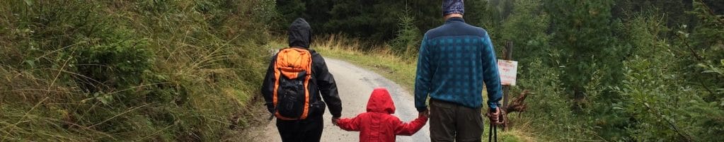 Family with young child walks down trail wearing winter clothing